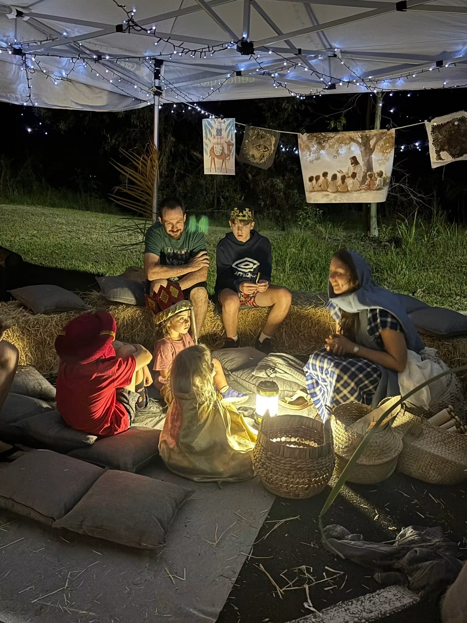 Visitors resting on cushions among woven baskets, lit by a single lantern after dark