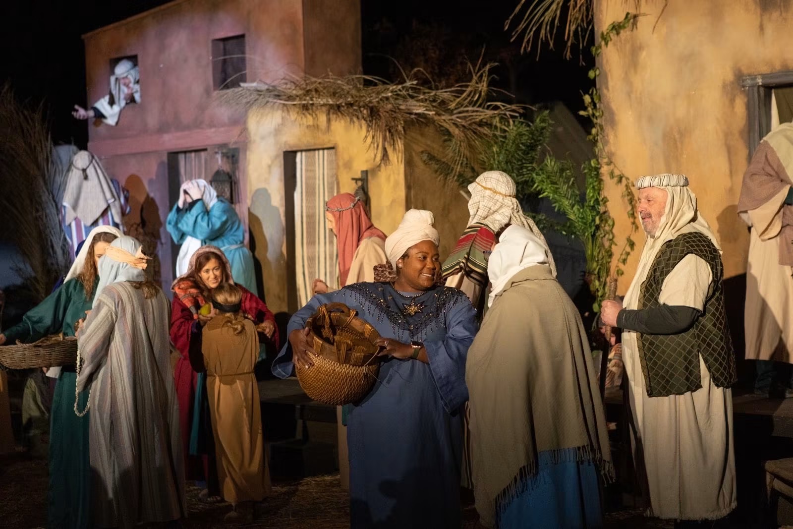 Villagers in costume at a market stall, one carrying a basket of bread