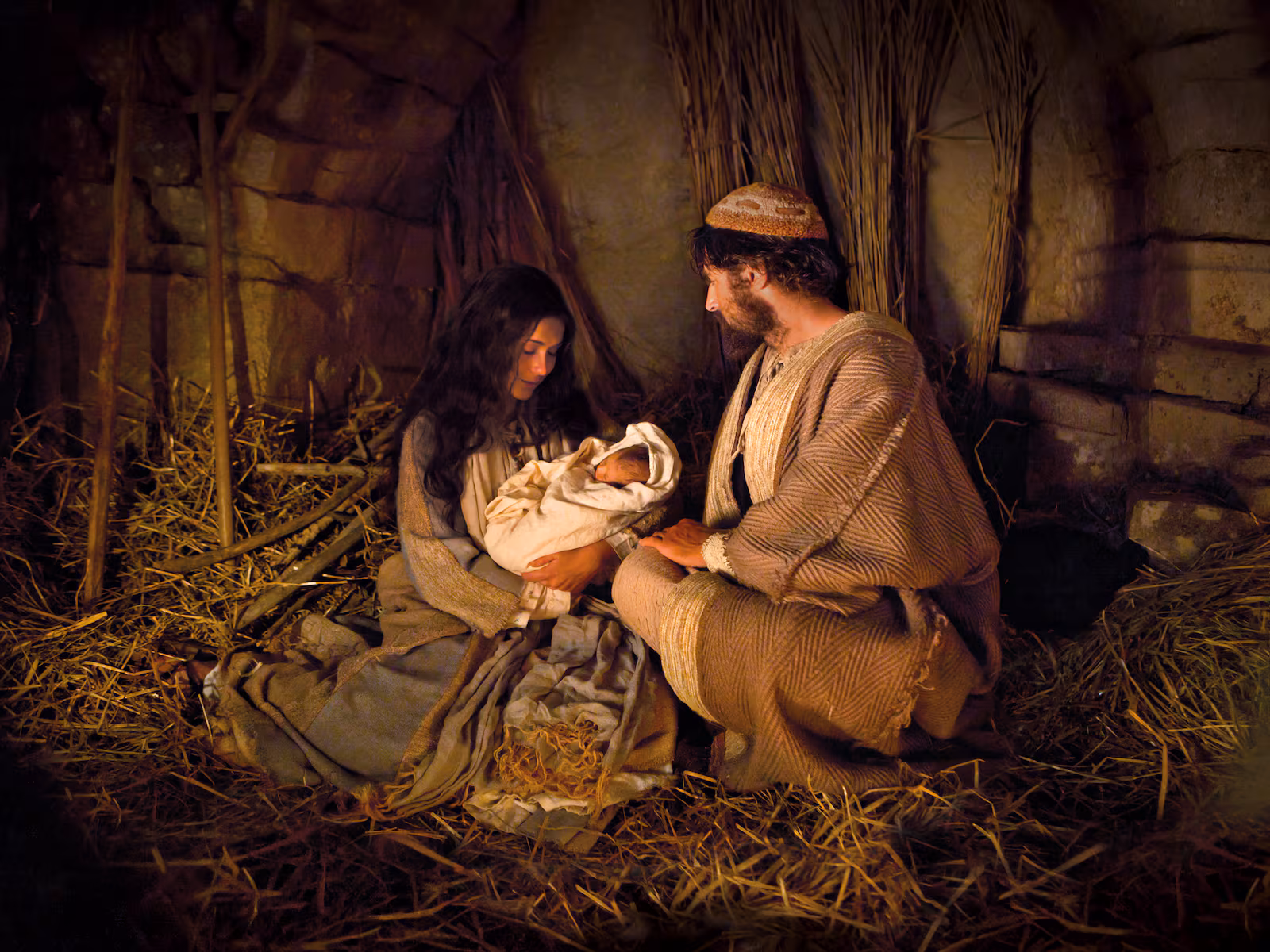 Mary and Joseph kneeling beside the newborn Jesus on the straw of a lamplit stable